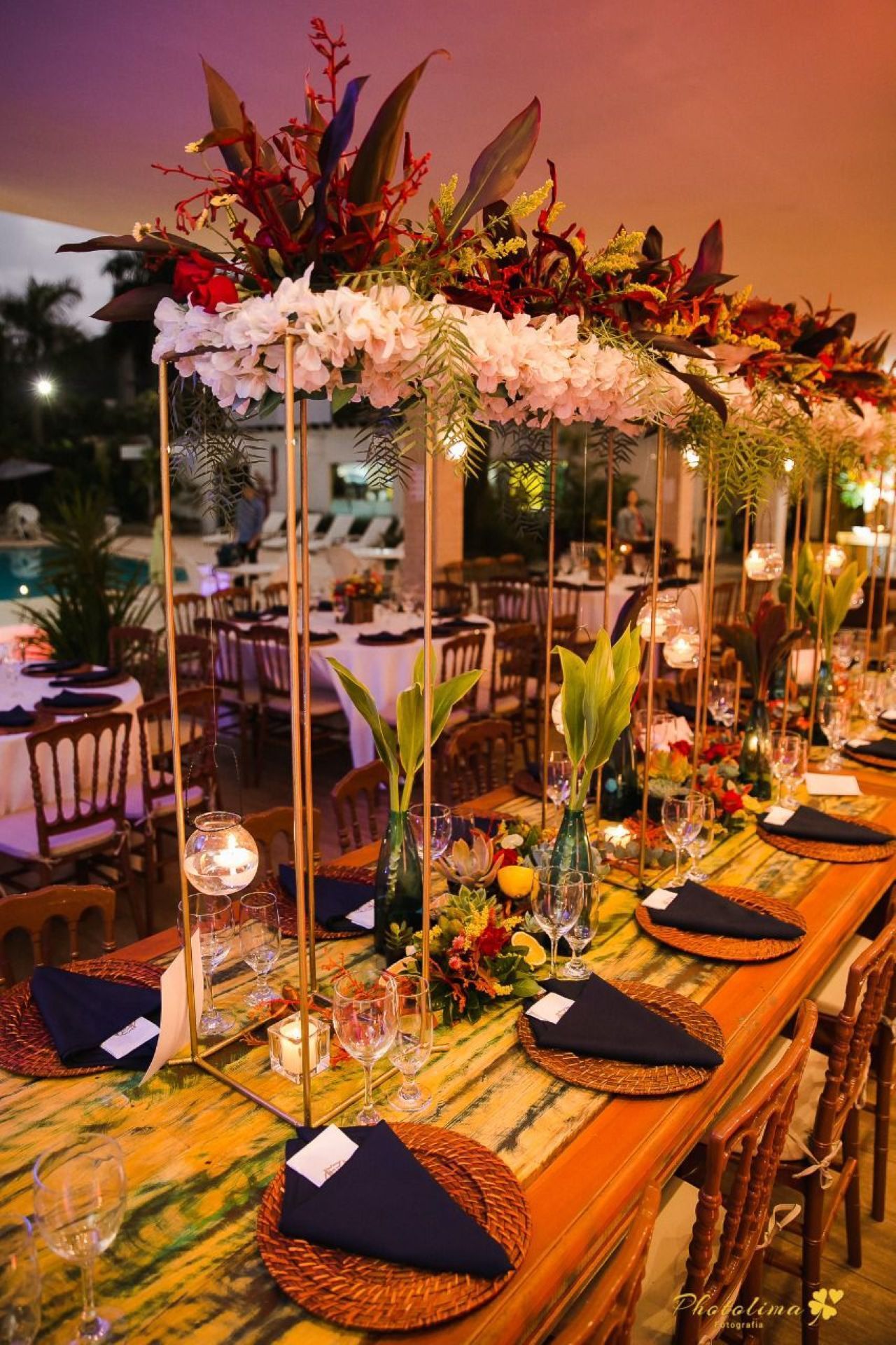 Mesa de jantar comprida posta para um evento com arranjos florais de centro de mesa, velas e lugares marcados.