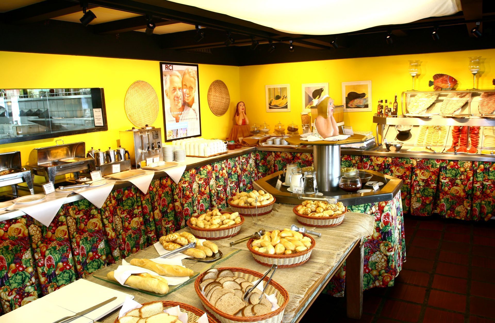 Buffet com diversos itens alimentícios expostos em uma sala amarela vibrante.