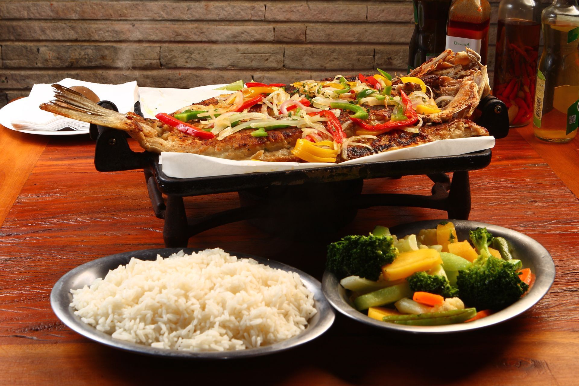 Peixe inteiro grelhado com arroz e legumes servido sobre uma mesa.