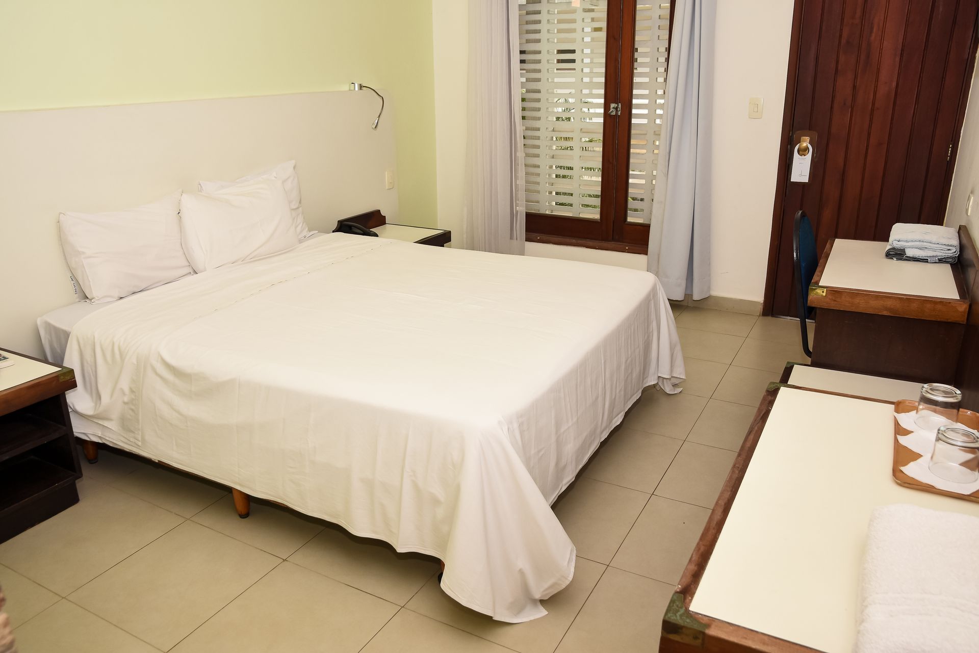 Quarto de hotel com uma cama grande, mesas de cabeceira e uma porta que dá para uma varanda.
