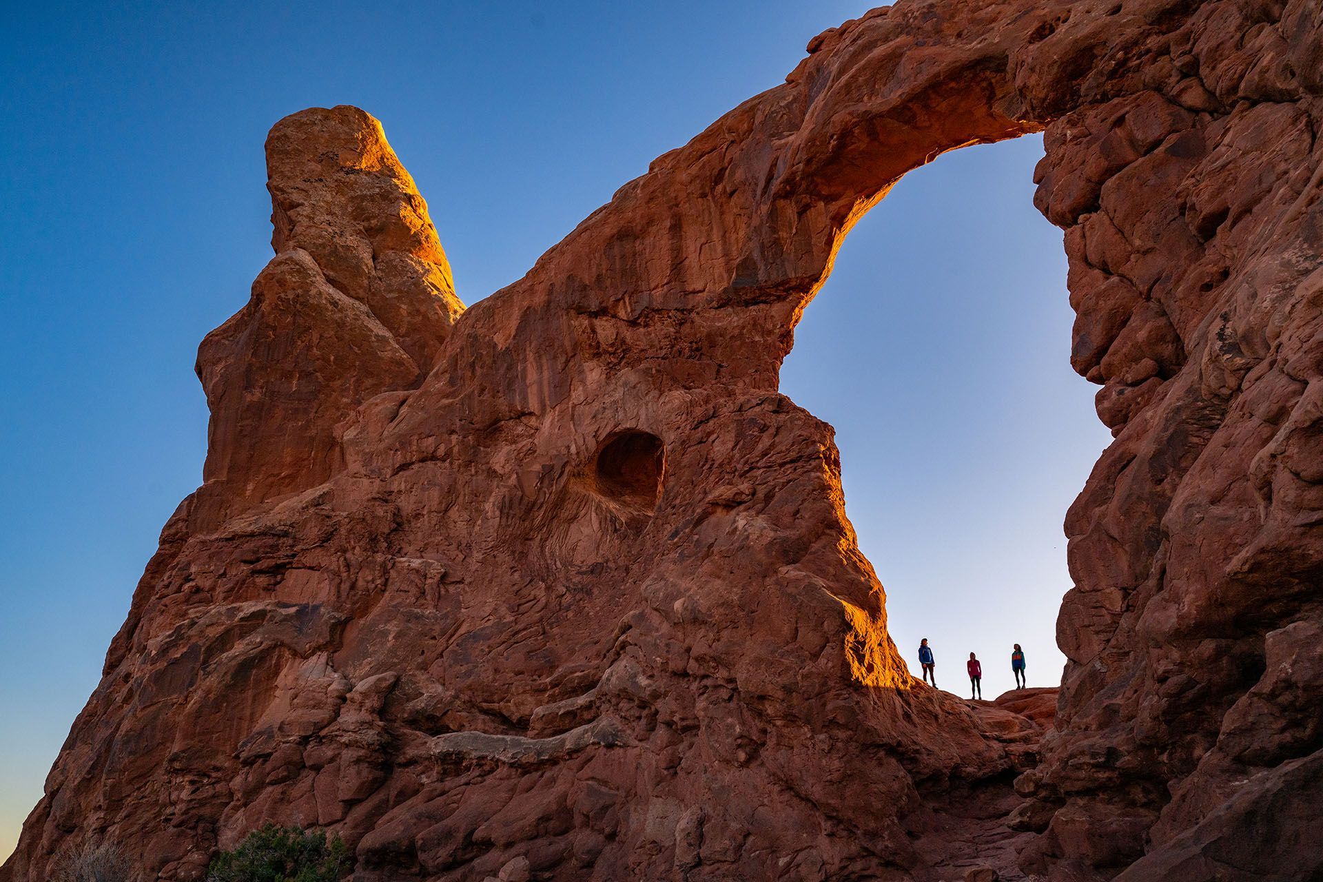Red rock arch with three silhouetted figures on top; Arches National Park.