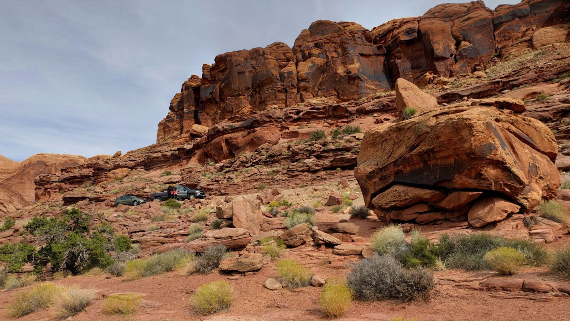 Red rock landscape with large boulder in foreground, blue sky above.