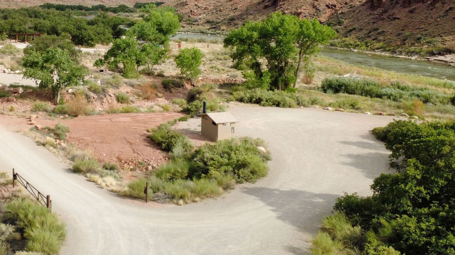 A gravel parking area next to a river with trees and a small restroom.