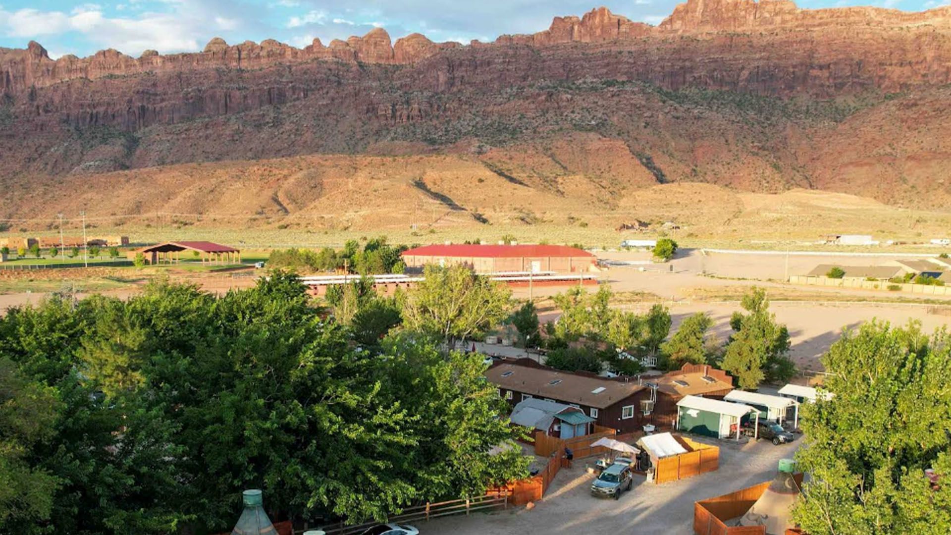 Campground with RVs and trees, red rock mountains in the background.