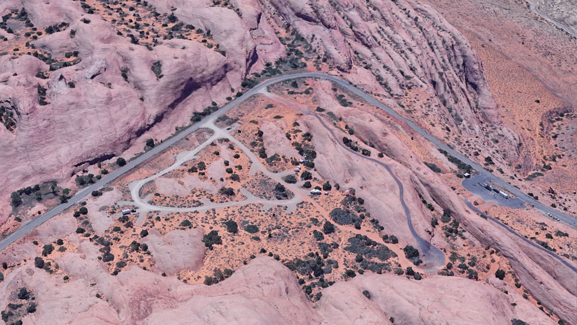 Overhead view of a winding road through pink sandstone formations with parking areas and sparse vegetation.