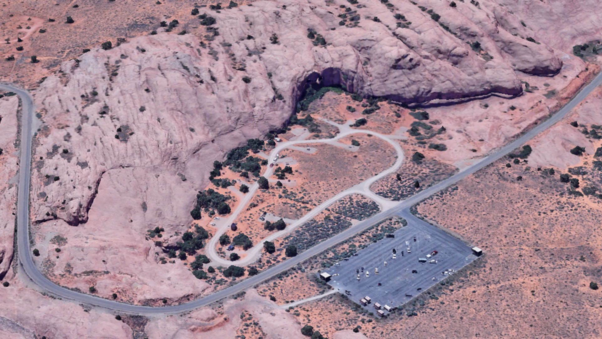Aerial view of a desert landscape with a winding road, parking lot, and a heart-shaped trail.