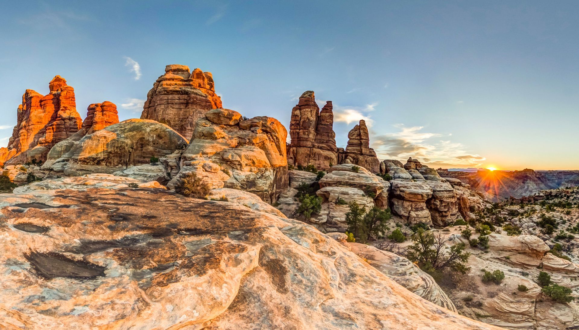 Sunset illuminates sandstone rock formations in a desert landscape.