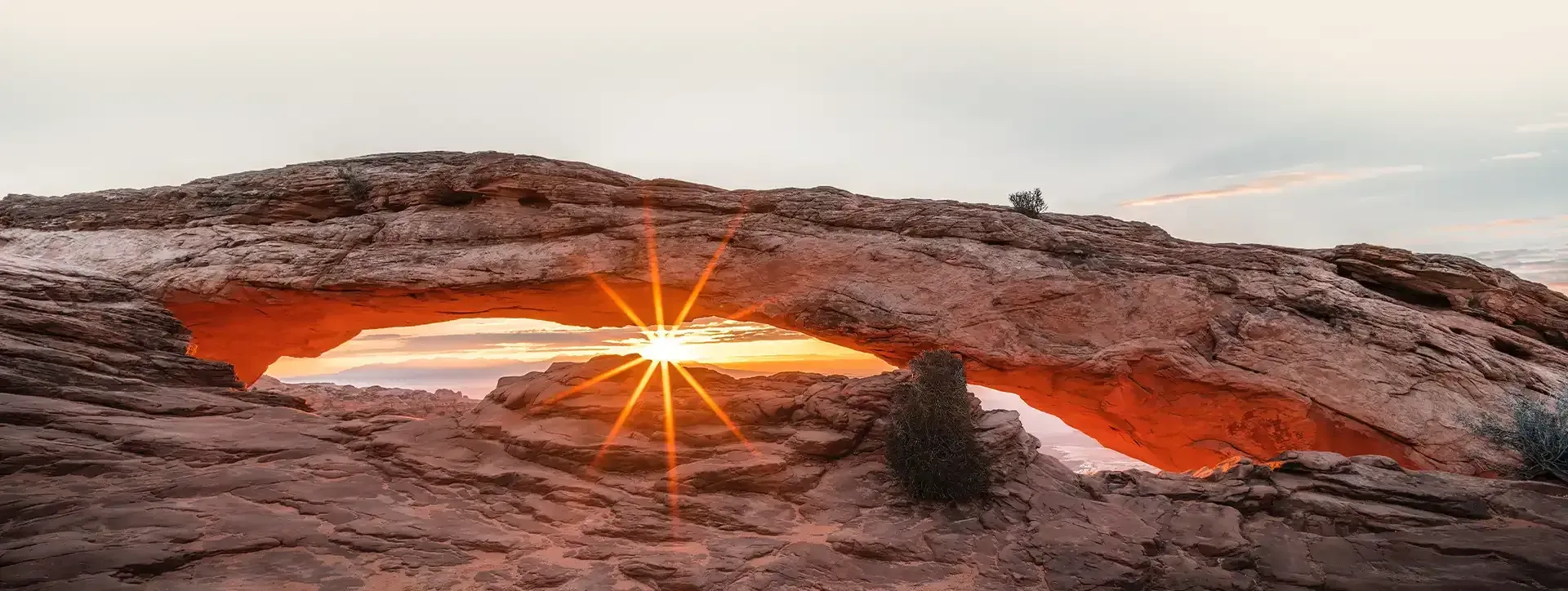 Sunset through Mesa Arch in Canyonlands National Park, Utah, illuminating red rock formations.