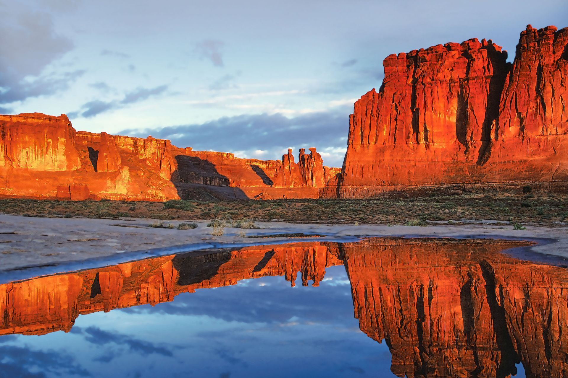 Red rock formations reflect in a pool of water at sunset.