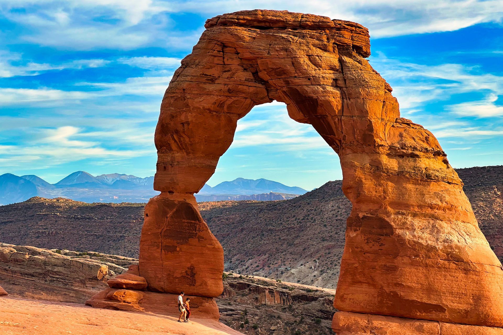 Delicate Arch in Arches National Park, Utah. Red rock formation with blue sky, some mountains in the background.