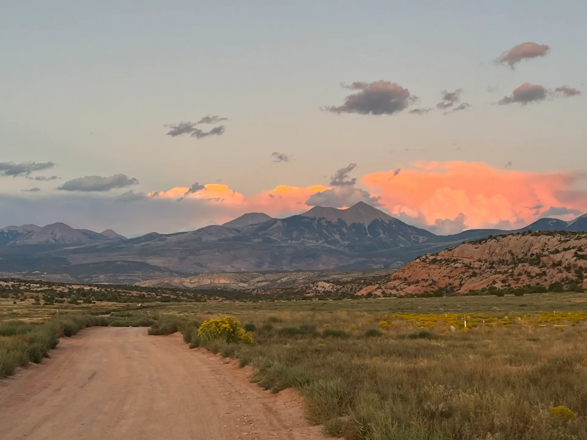 Dirt road leading toward mountains at sunset. Pink and purple clouds in the sky.