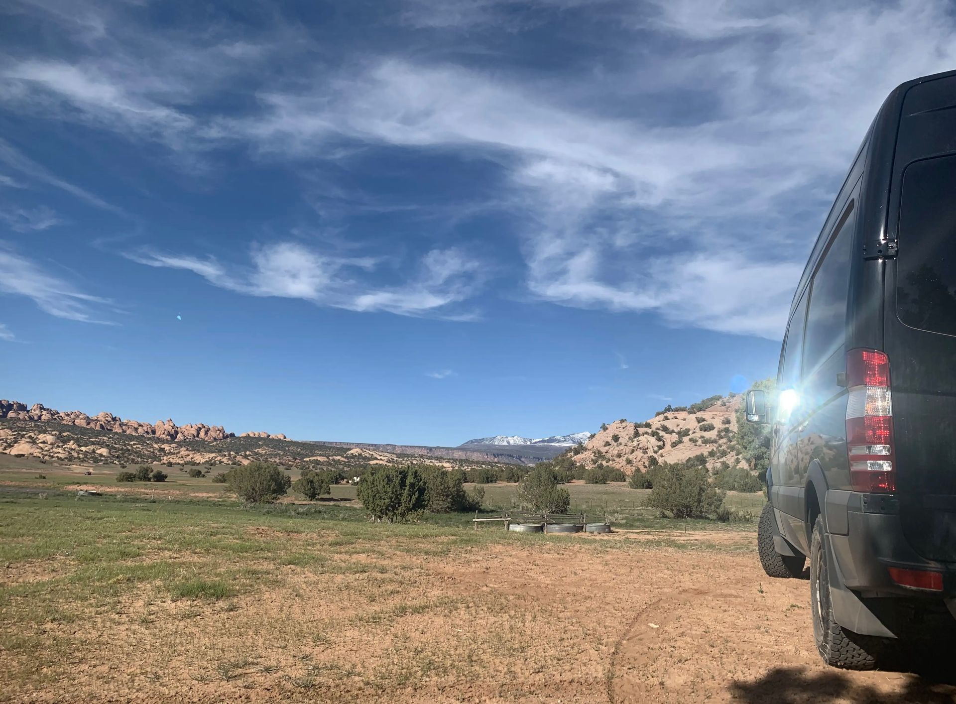 Black van parked on dirt road, scenic desert vista under a blue sky with scattered clouds.