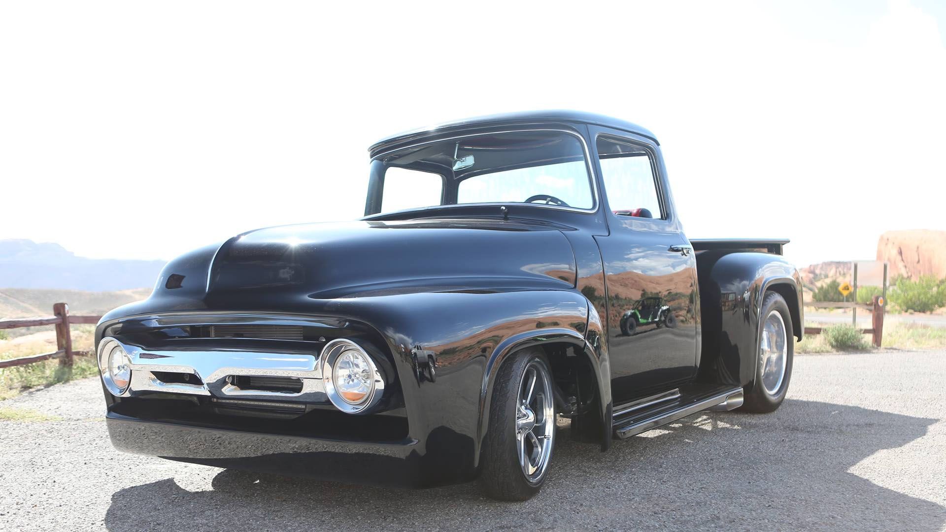 Black classic Ford pickup truck parked in front of a mountain landscape.