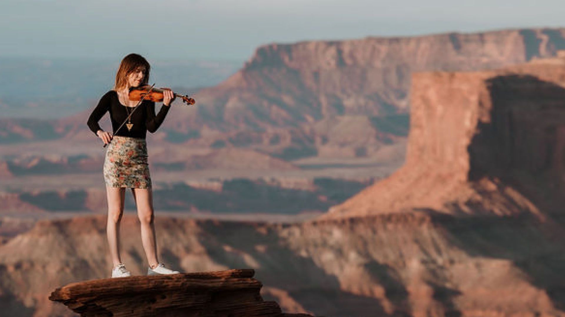 Woman plays violin on a rock ledge overlooking a desert canyon.