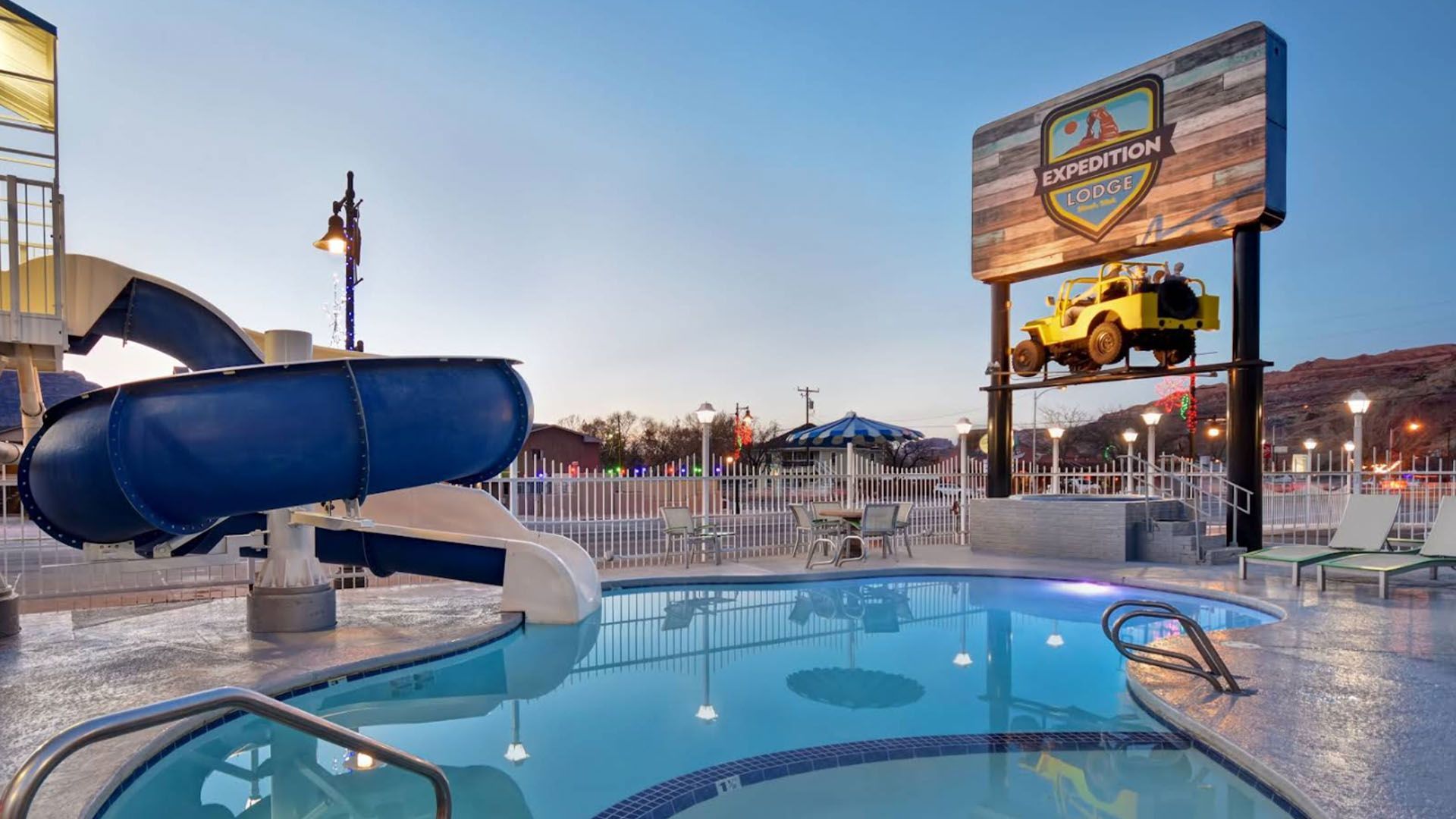 Pool with a blue water slide and sign with a yellow jeep.