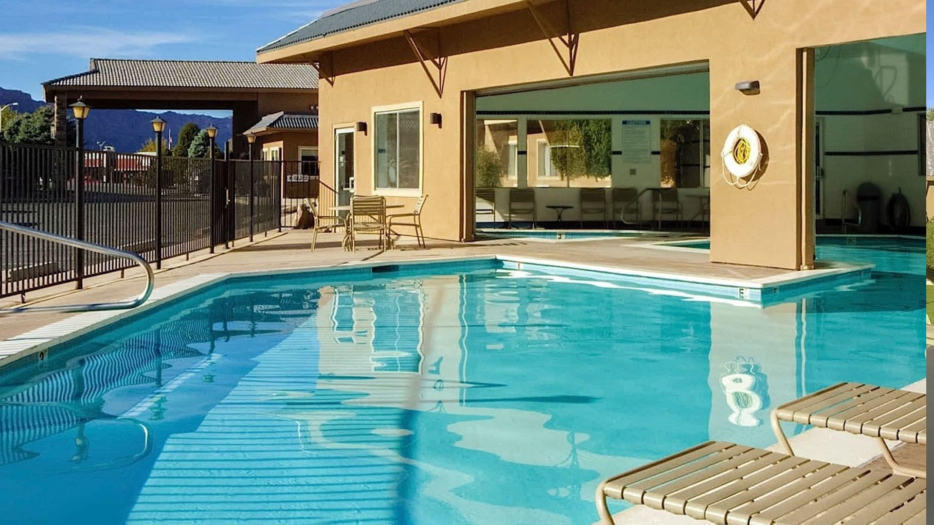 Pool with turquoise water next to a building with an open glass wall; lounge chairs are visible.
