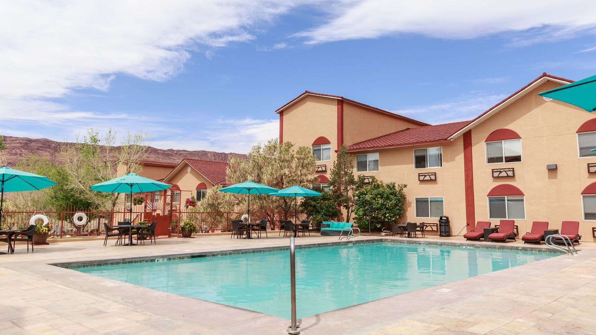 Pool with turquoise water at a beige hotel with teal accents under a blue sky.