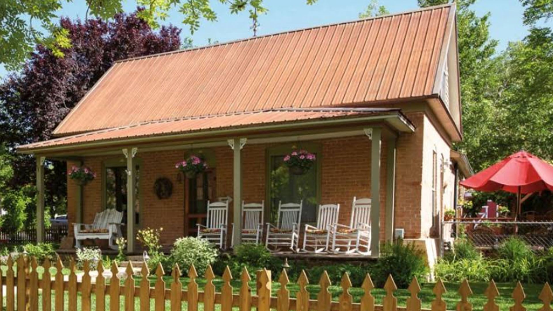 Historic brick house with porch, rocking chairs, and red umbrella in a garden.