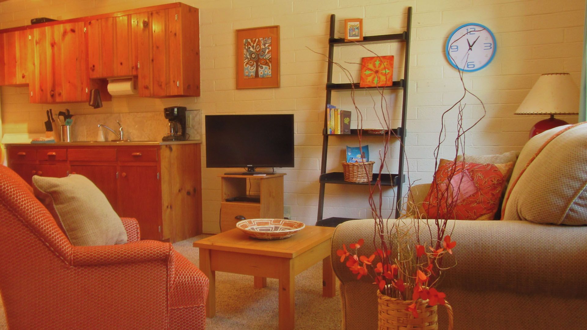 Cozy living space with orange cabinets, a couch, armchair, and a wooden shelf with decor.