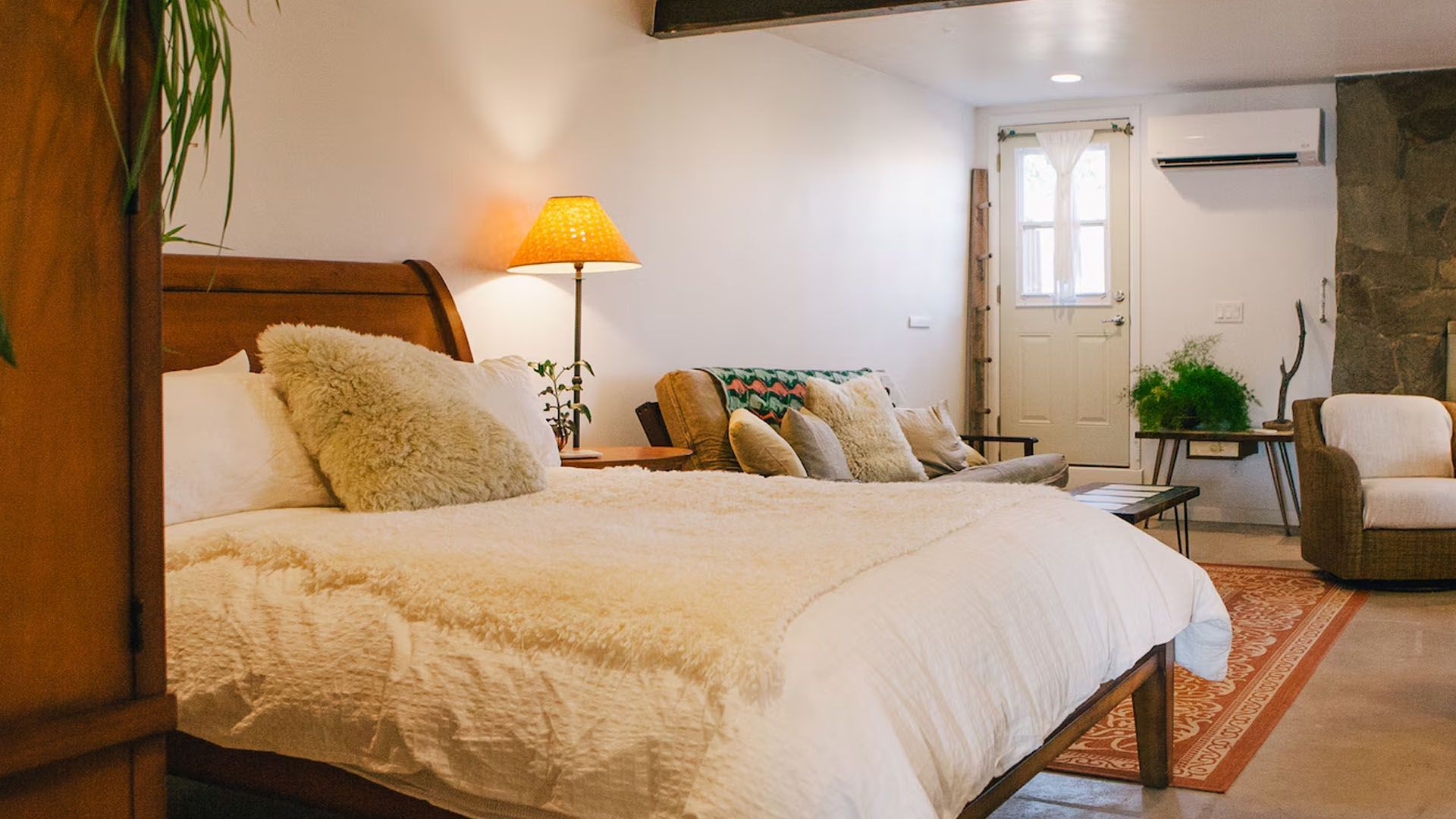 Cozy bedroom with a bed, sofa, and floor lamp. Sunlight streams in.