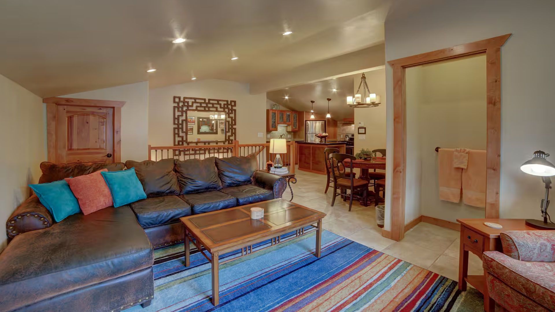 Living room with brown leather sectional sofa, colorful rug, open to dining area.