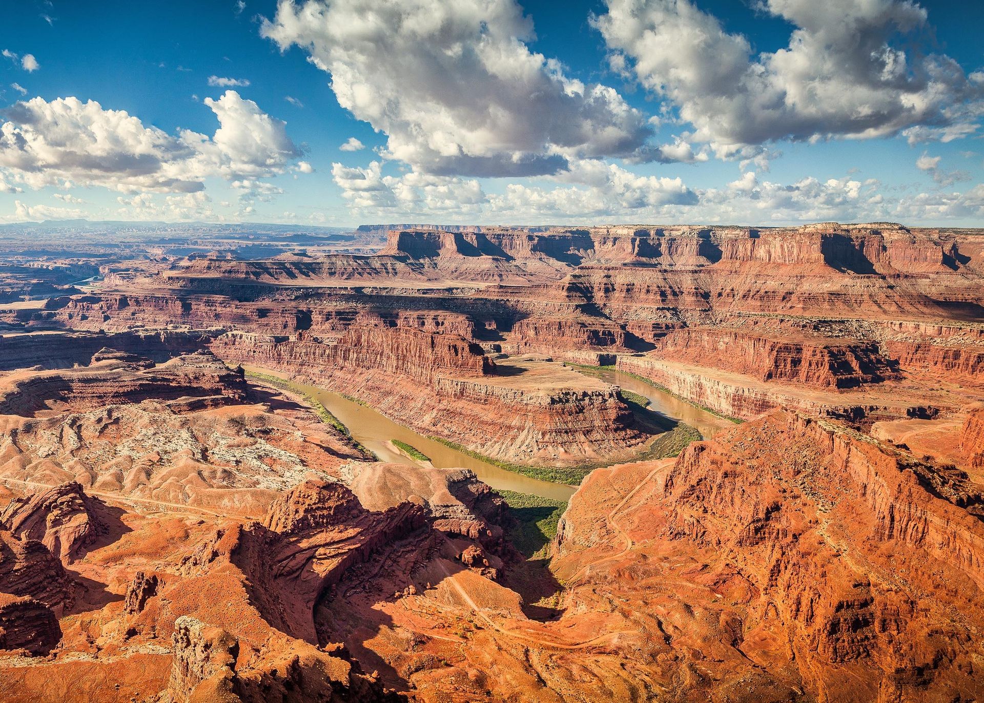 Red rock canyon landscape with a winding river under a partly cloudy blue sky.