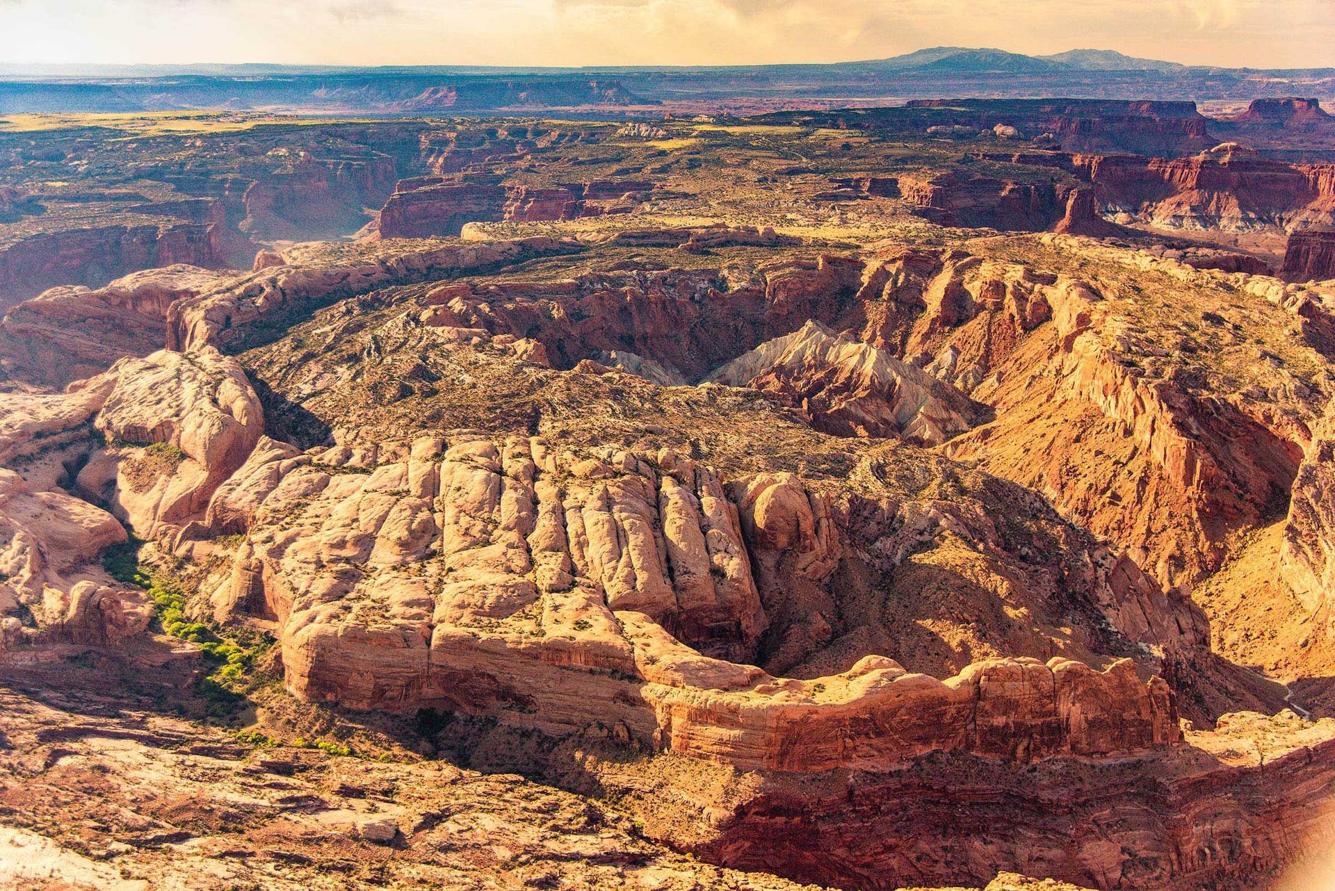 Panoramic view of a desert canyon, reddish-brown rock formations and sparse green vegetation.