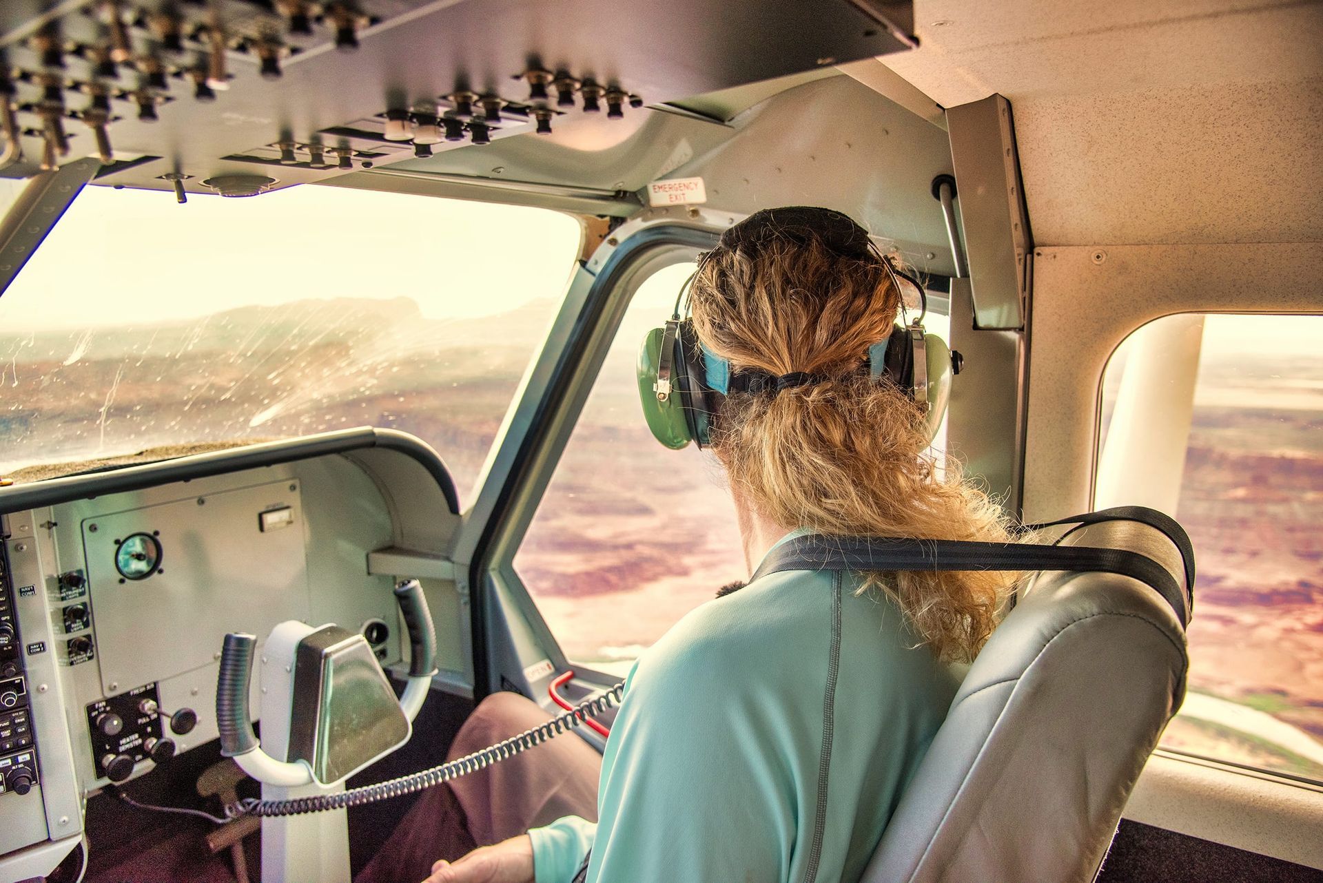 Passenger in a small plane, wearing headset, looking out window at landscape.