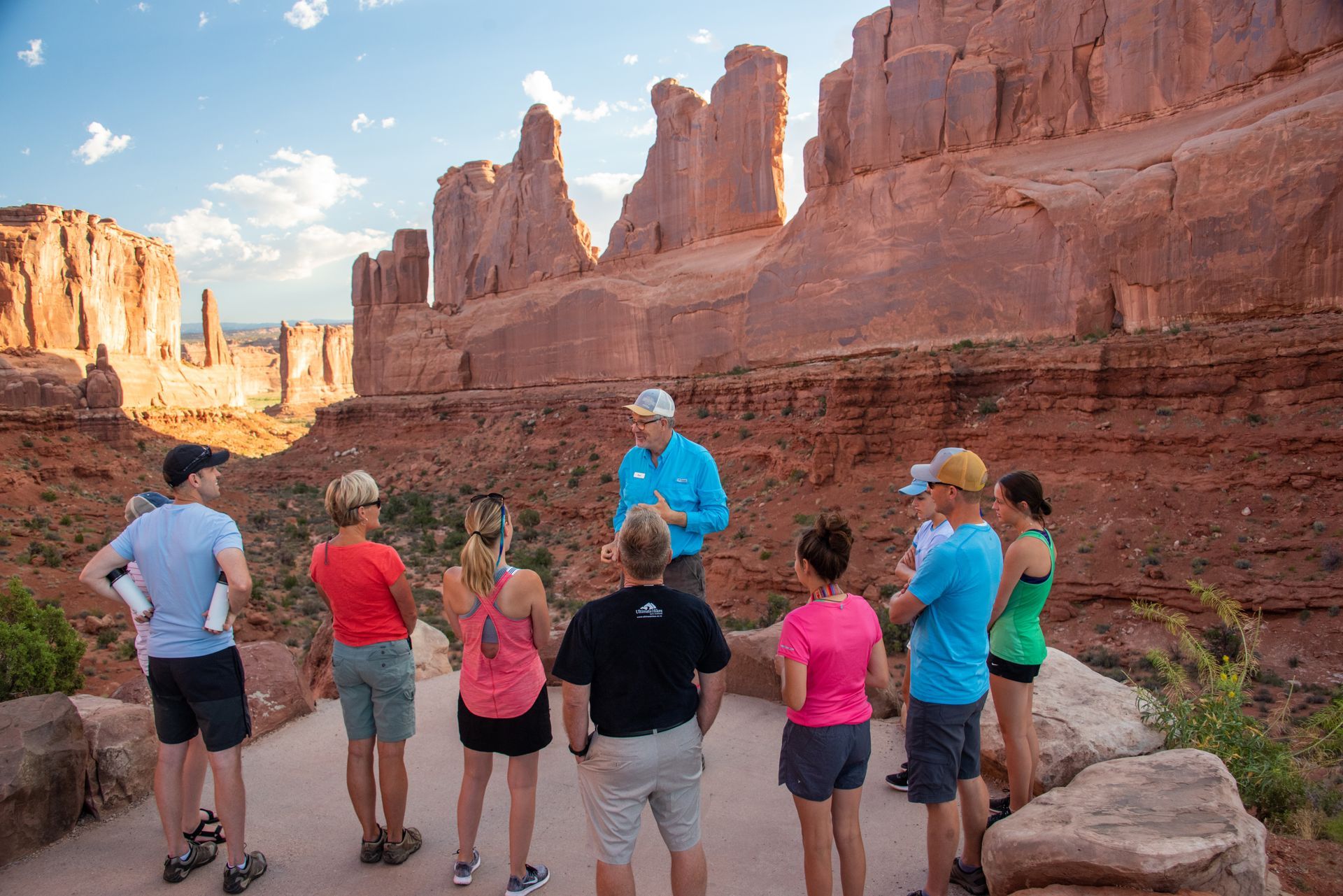 A group of people are gathered around a guide telling a story in Arches National Park.