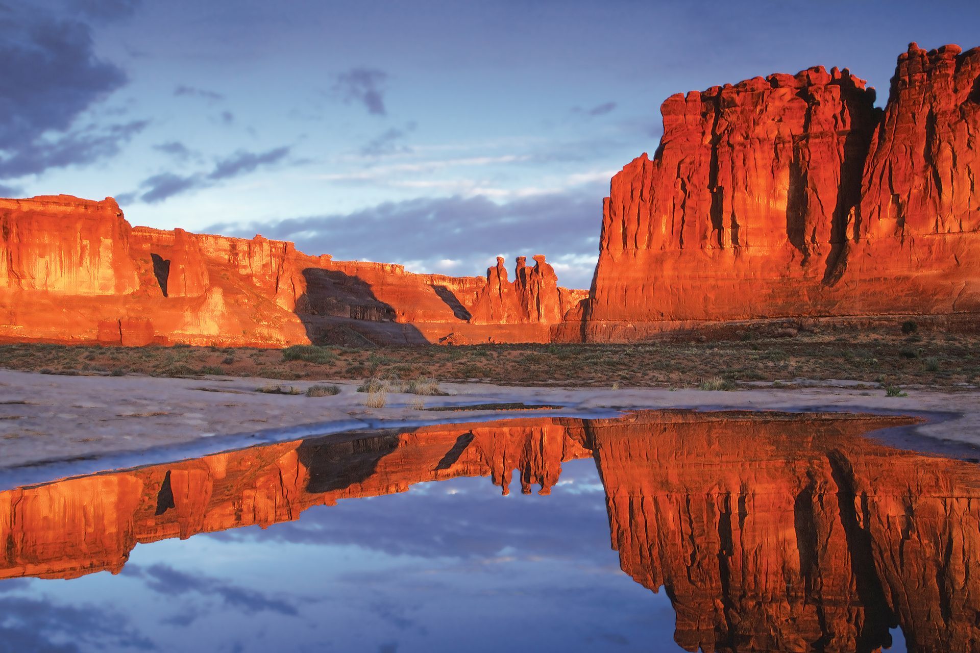 Red rock formations reflected in still water under a blue sky at sunset.