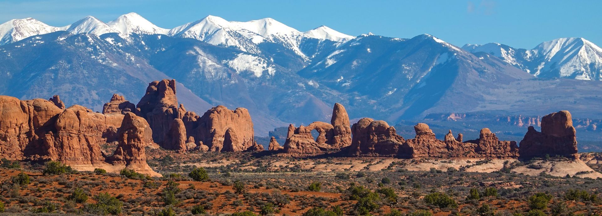 Red rock formations and mountains with snow caps under a blue sky. Desert landscape.