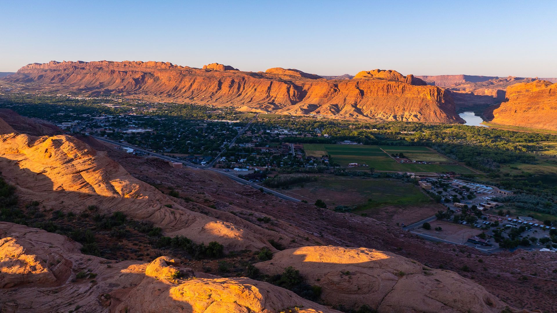 Red rock cliffs overlooking a town with a river at sunset.
