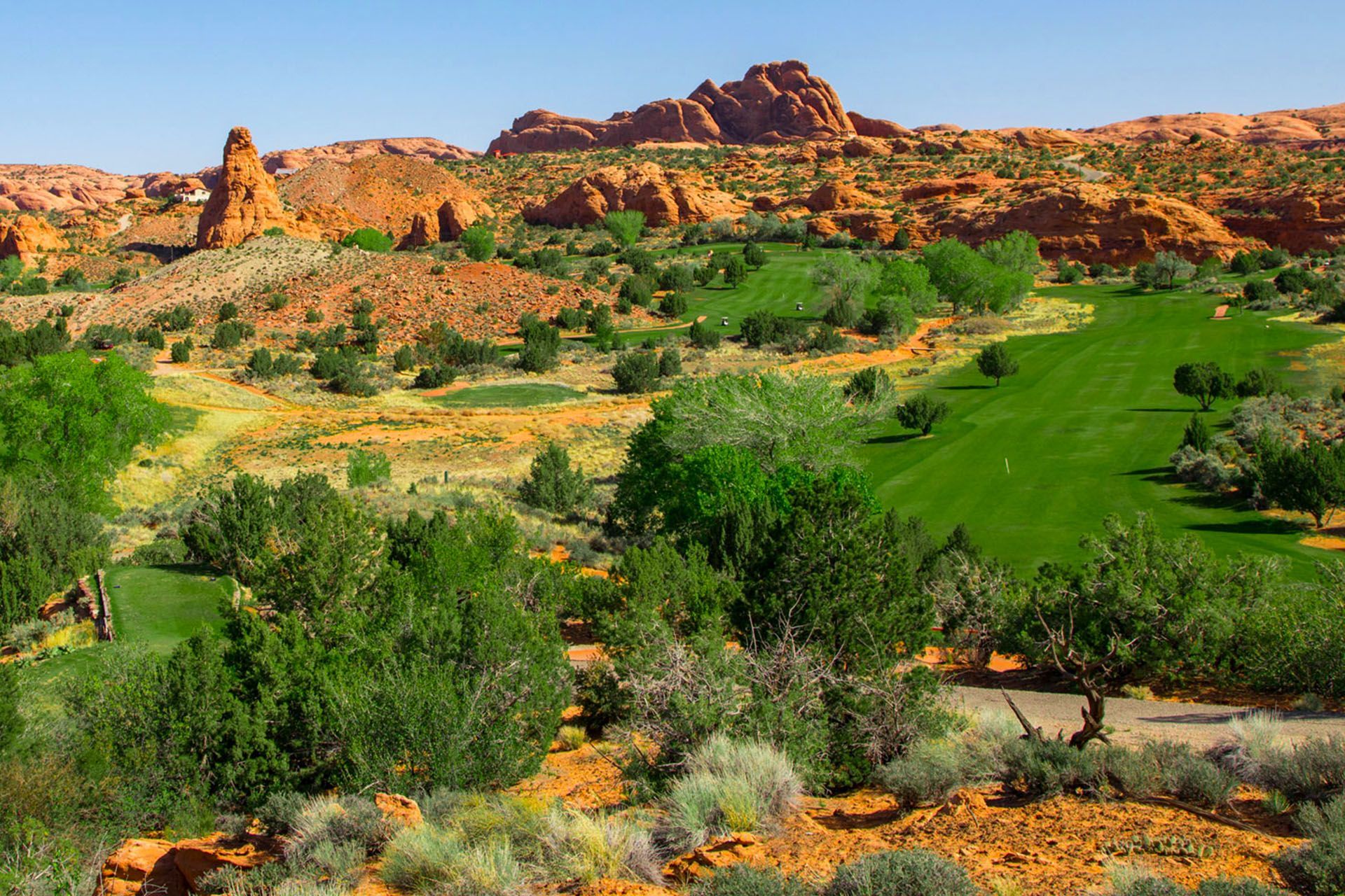 Moab Golf Course surrounded by green trees and sandstone cliffs.
