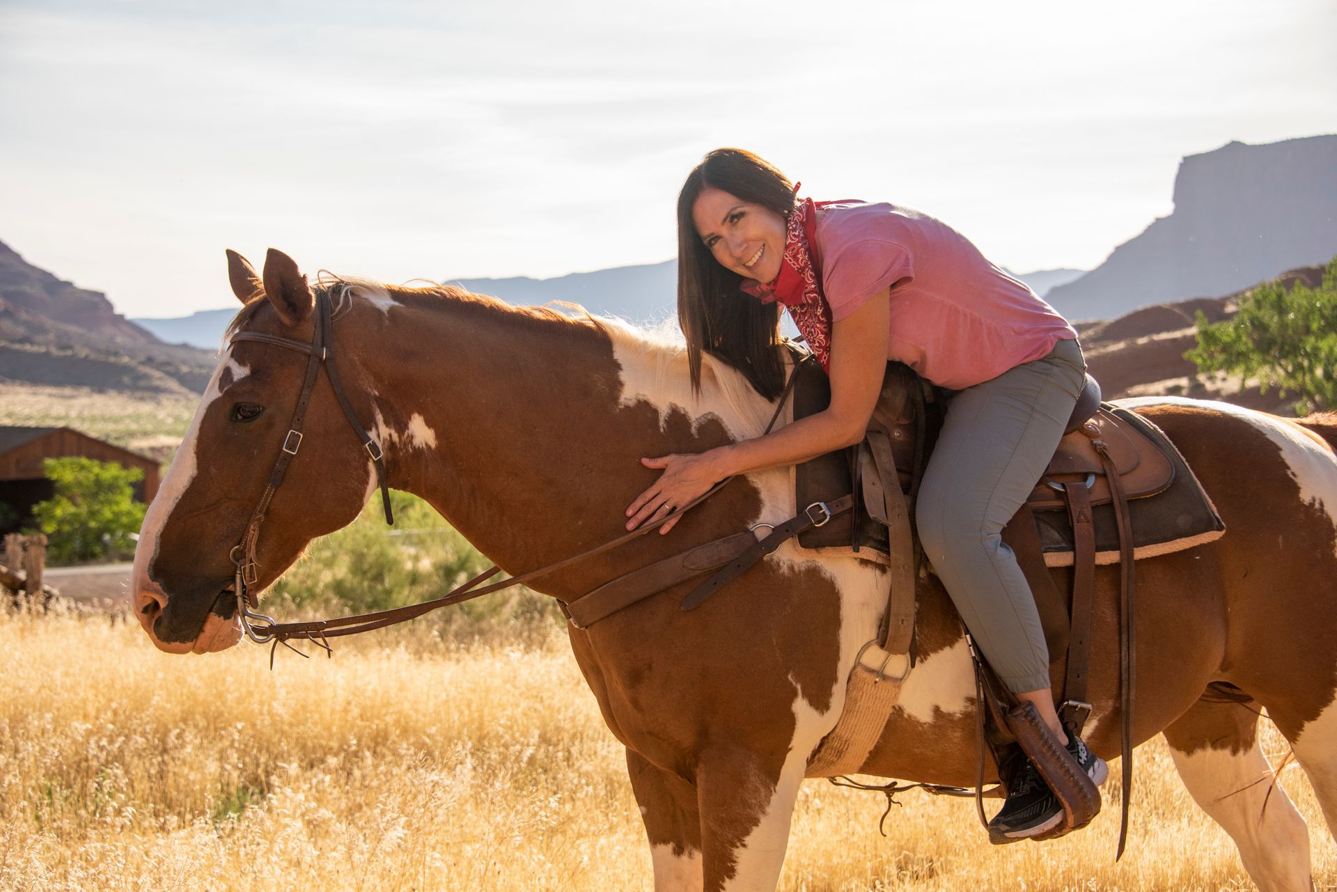 Woman hugging a paint horse in a desert setting; she smiles, wearing a red shirt and bandana.