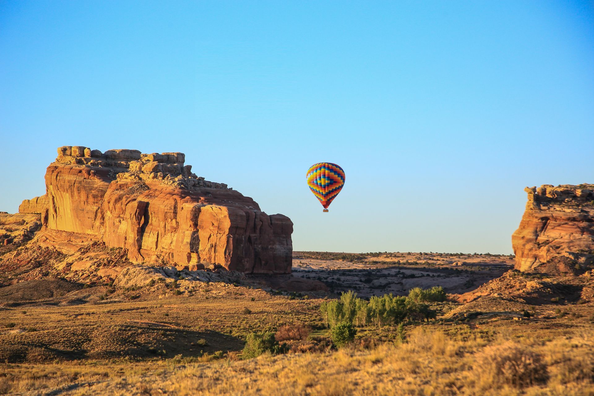 Hot air balloon over a desert landscape with mesas and blue sky.