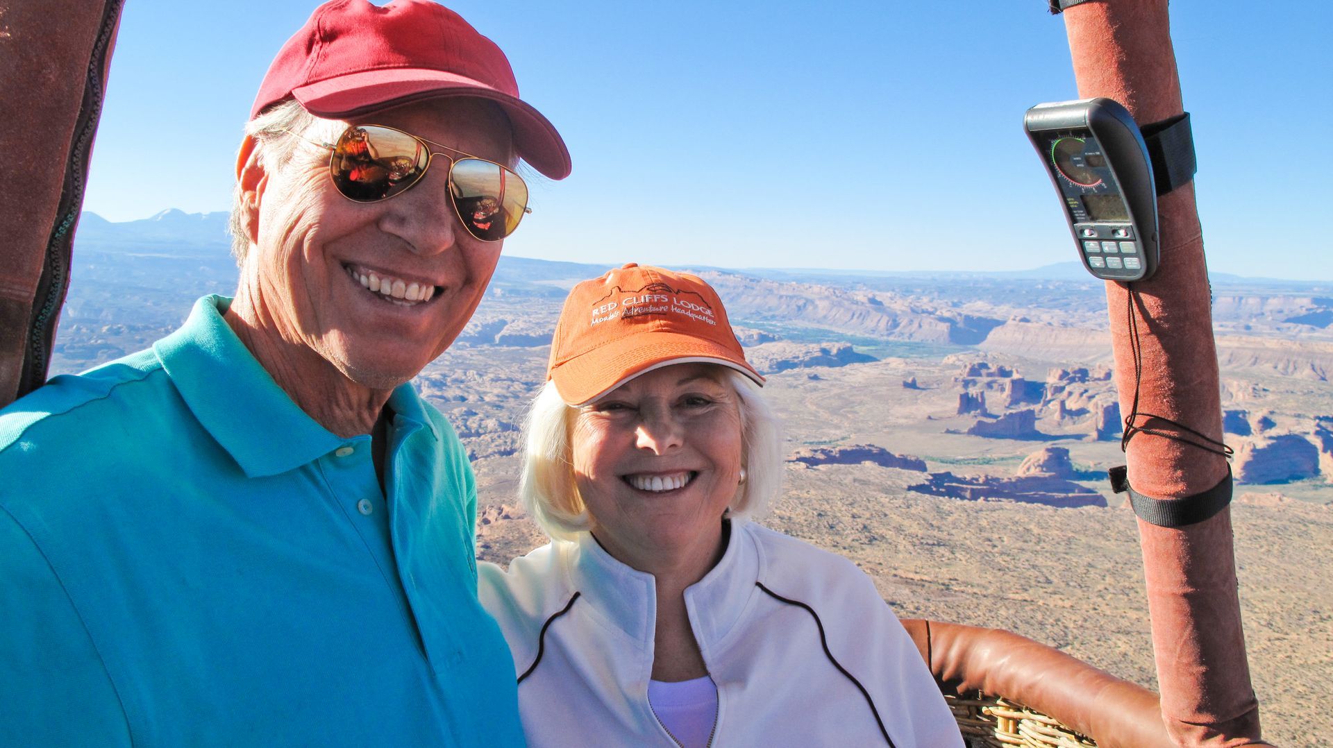 Couple smiling in hot air balloon basket over desert landscape. 