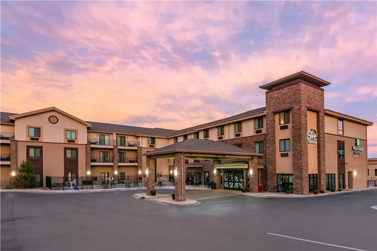 Hotel exterior under a pink and blue sunset. Brown brick, stucco building with a covered entrance.