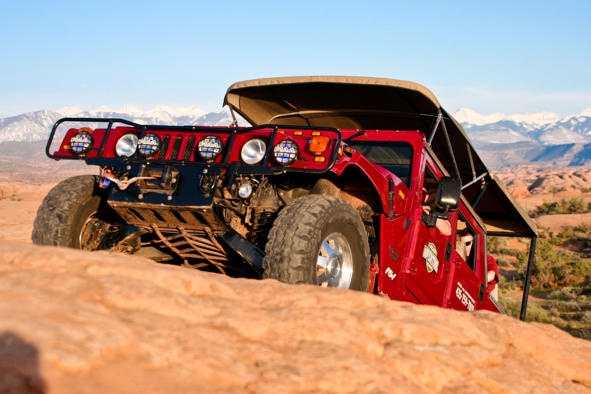 A red Hummer vehicle climbs up steep slickrock terrain on the Hell's Revenge Trail.