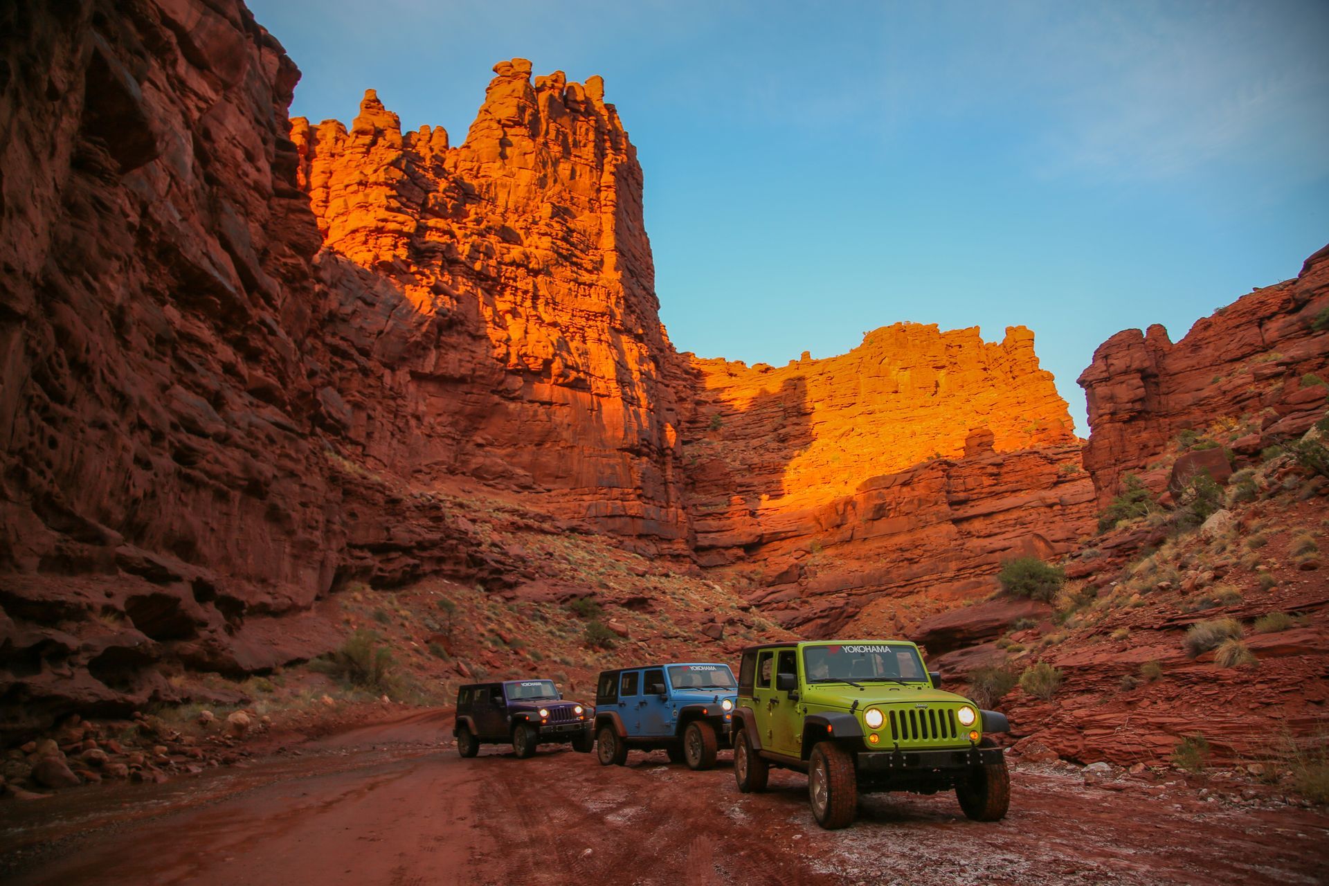 Four Jeeps driving through a red rock canyon at sunset.