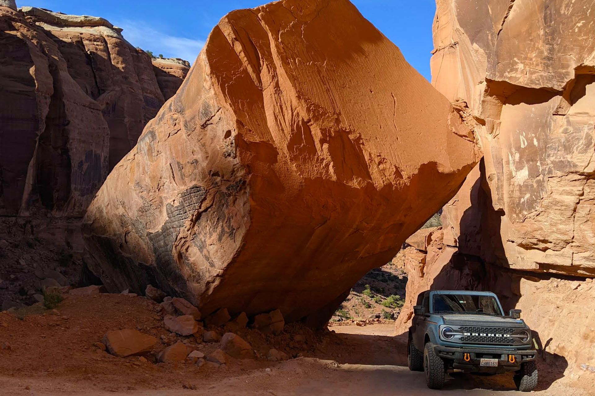 A bronco drives under a large boulder that has tipped against a cliff.