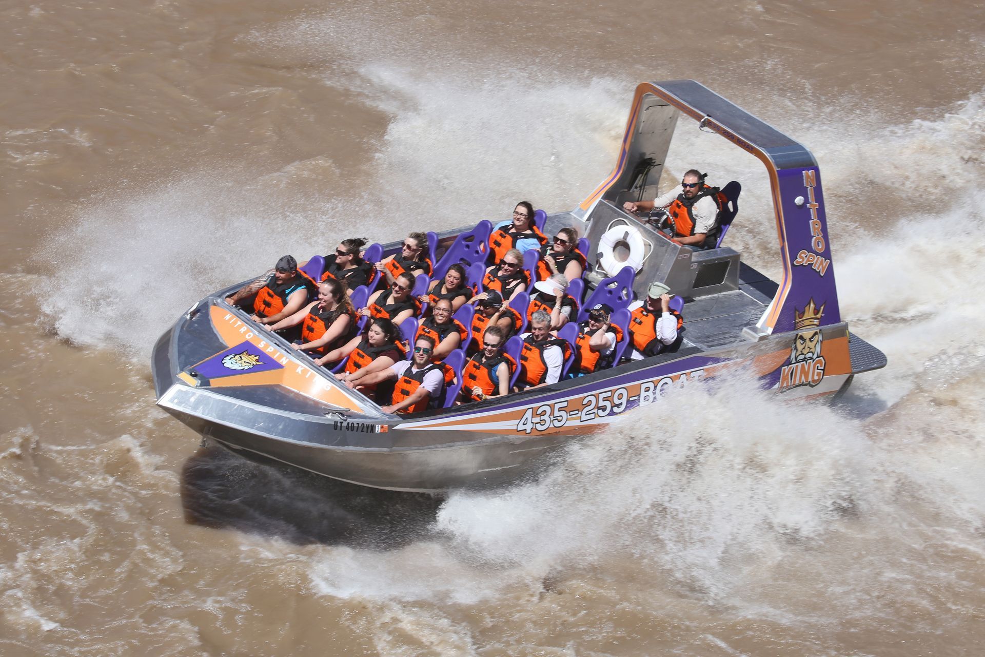 Jet boat with passengers navigating turbulent water, spraying white water. Orange and purple accents.