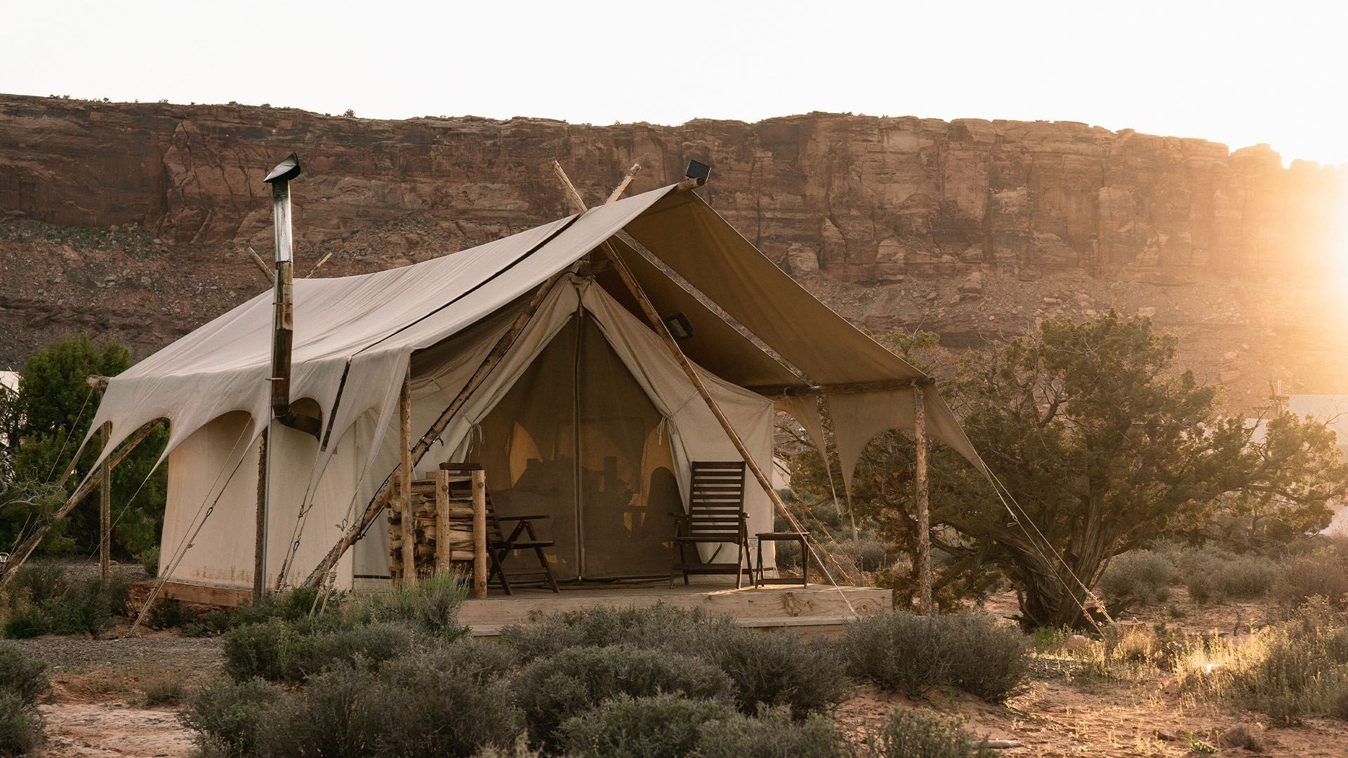 A camping tent sits in the desert with a cliff behind it.