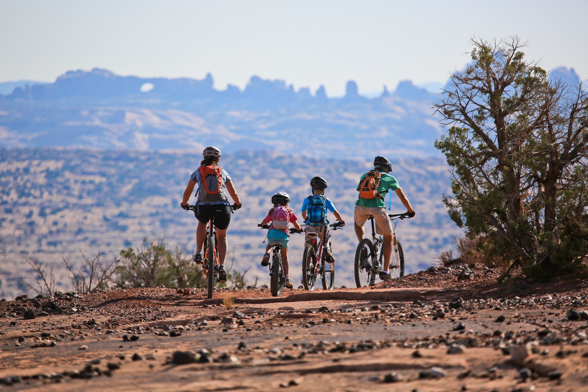 Family on mountain bikes, riding on a dirt trail overlooking a desert landscape.