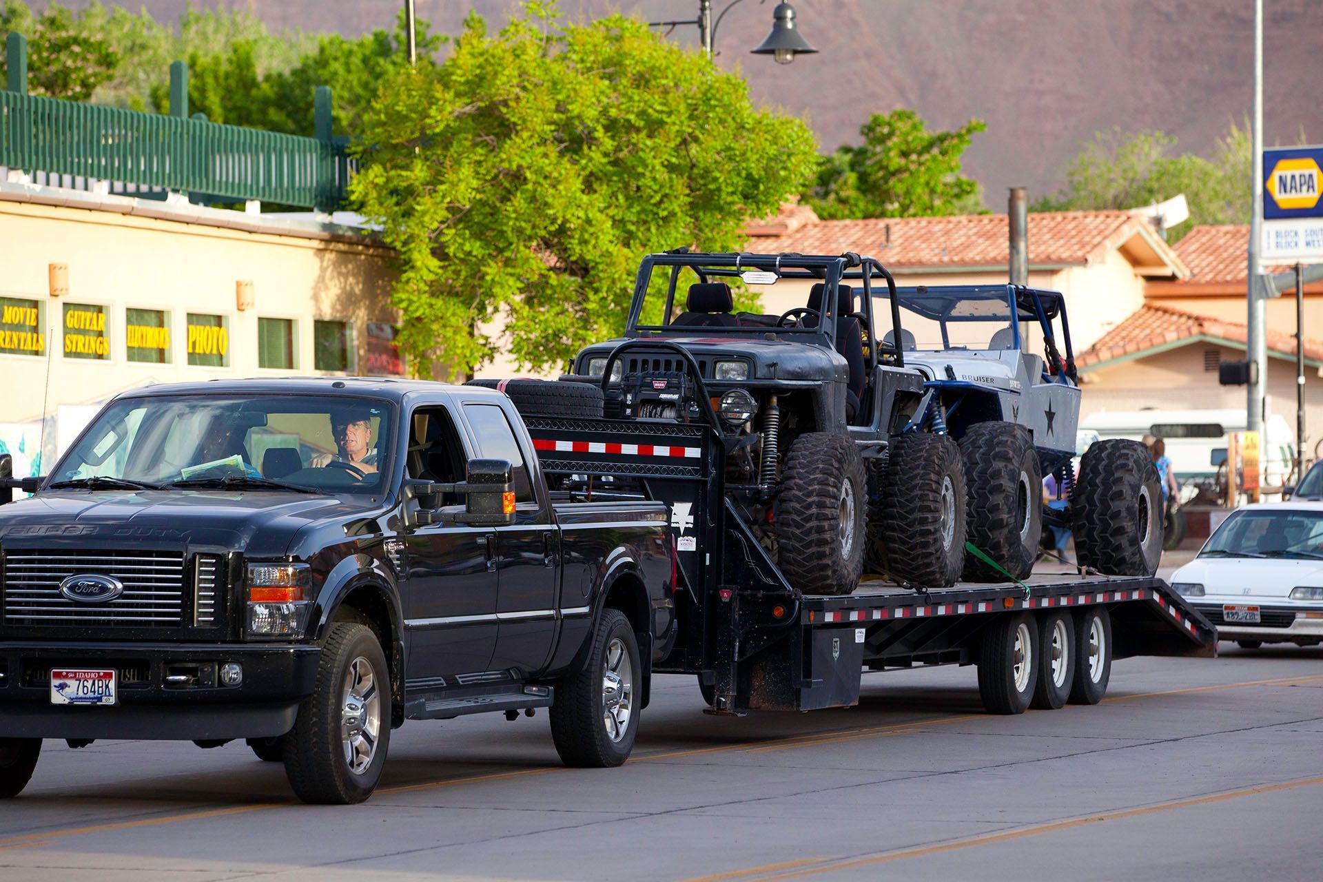 Black pickup truck towing a trailer with two black off-road Jeeps in a town.