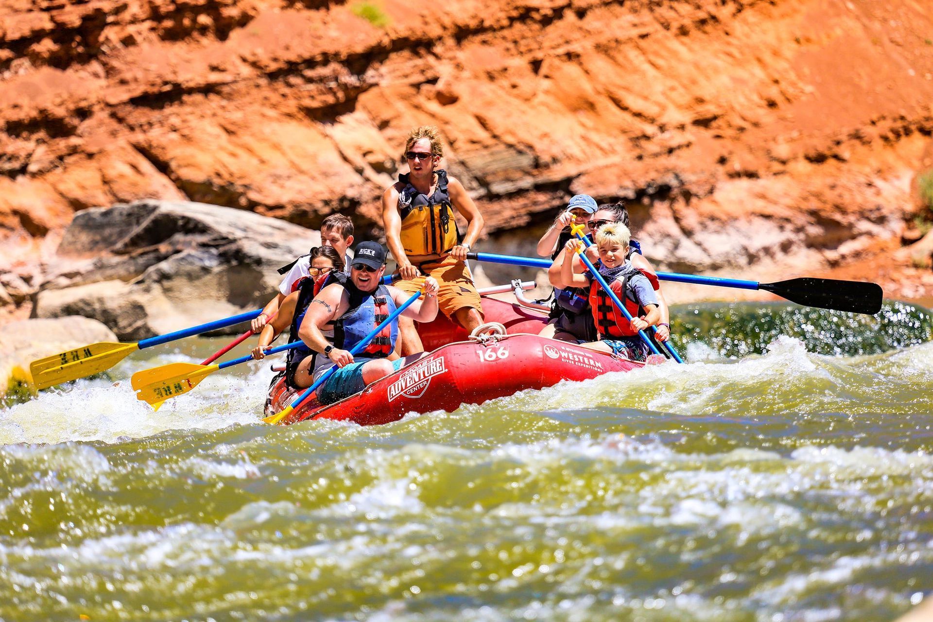 A family rafting on the Colorado River with green water, sandstone cliffs, and smiling faces.