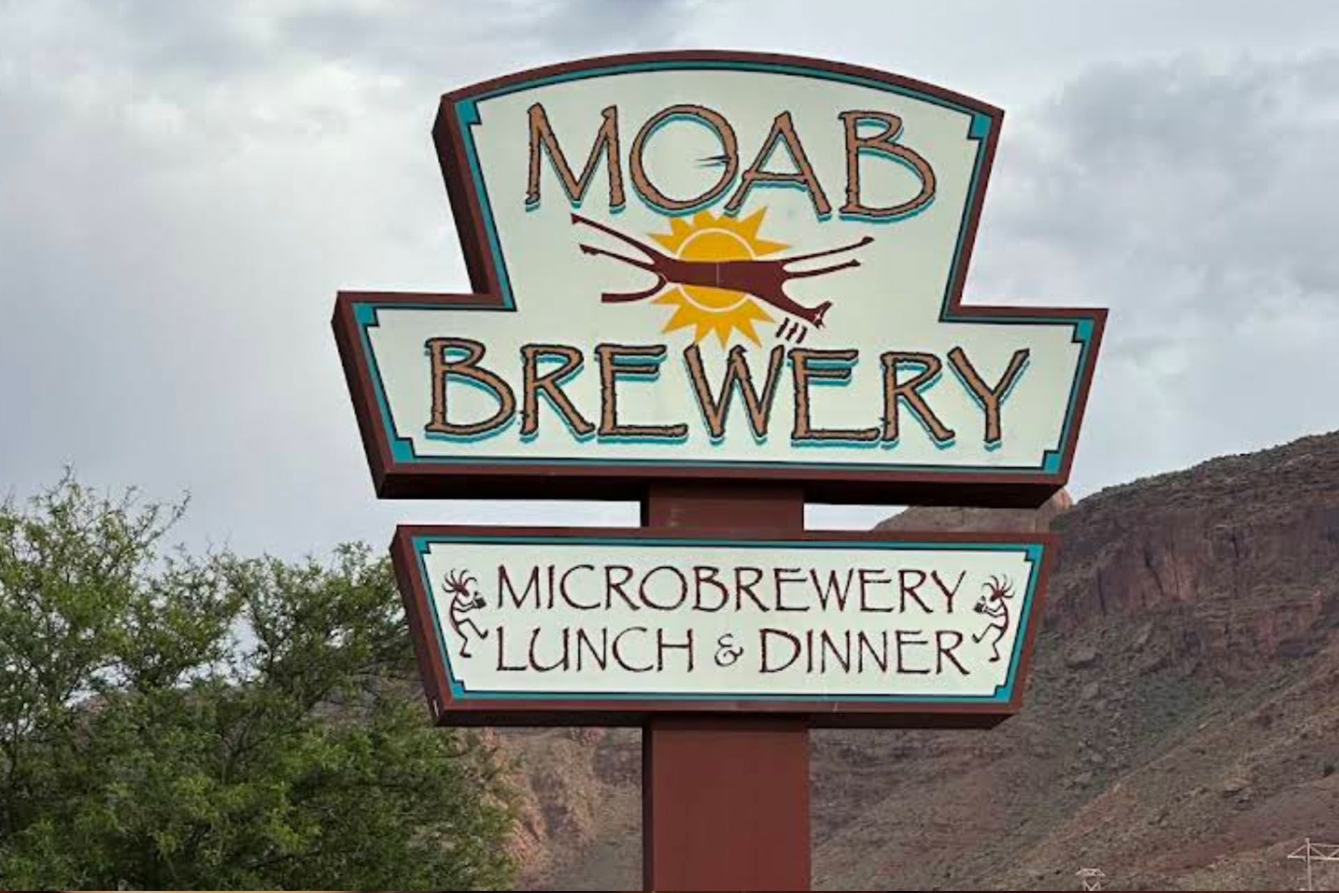 Moab Brewery sign, turquoise letters on cream, brown border, illustration of animal silhouette with sun.