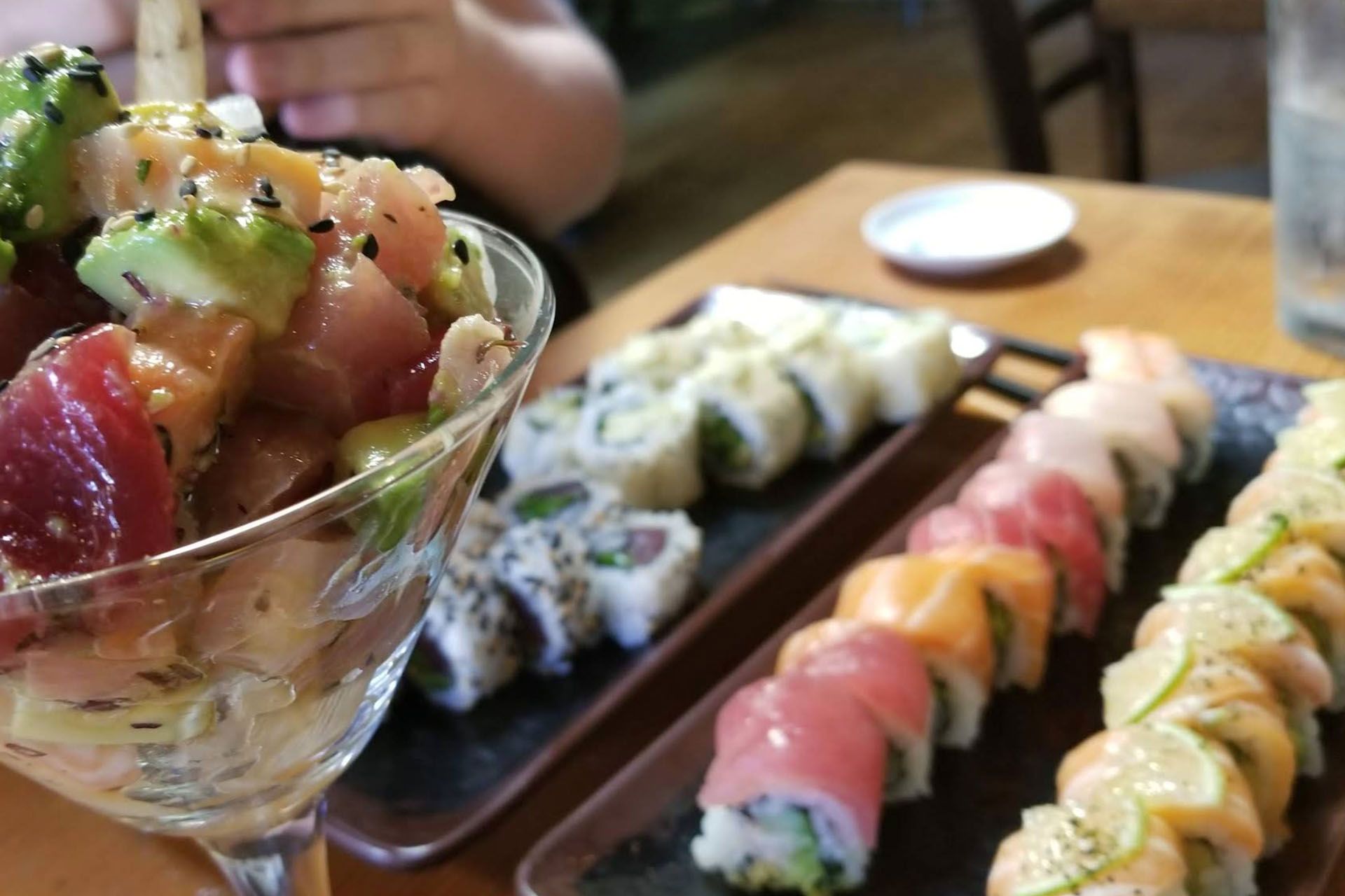 Sushi spread: a martini glass with tuna poke, and plates of colorful sushi rolls on a wooden table.
