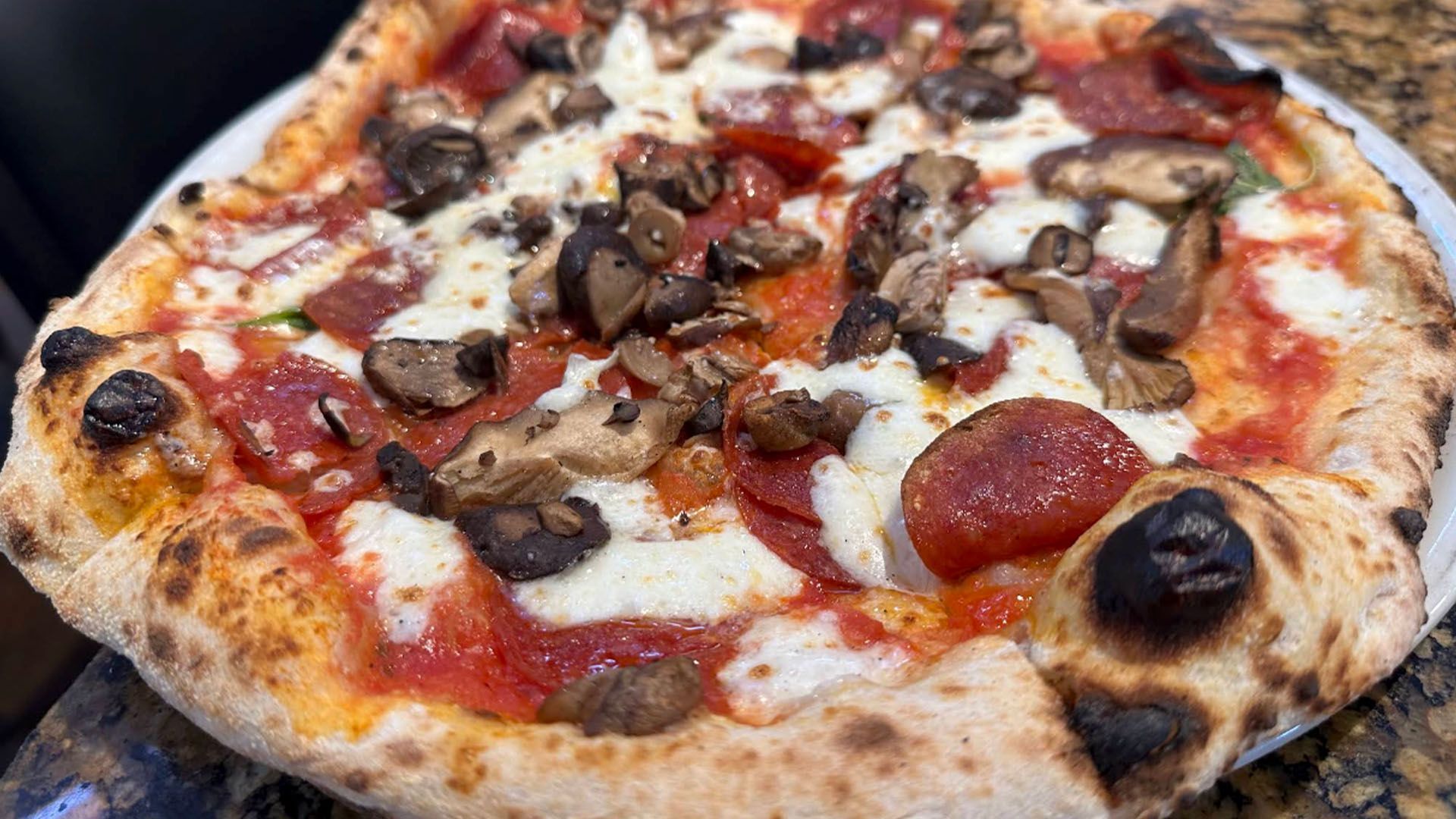 Pizza with pepperoni, mushrooms, and mozzarella cheese on a white plate.