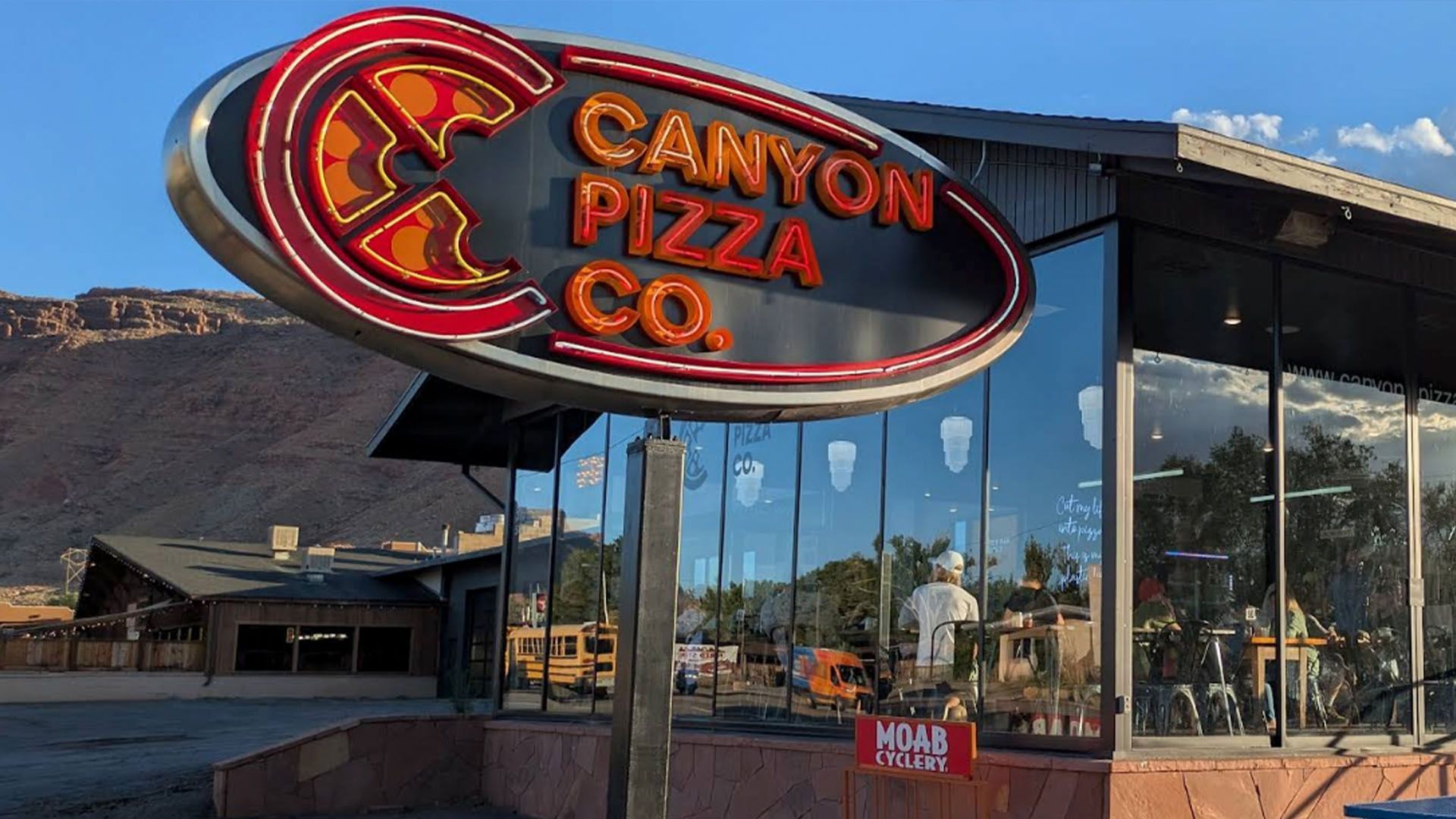 Canyon Pizza Co. sign with neon lights in front of a restaurant with a mountain backdrop.