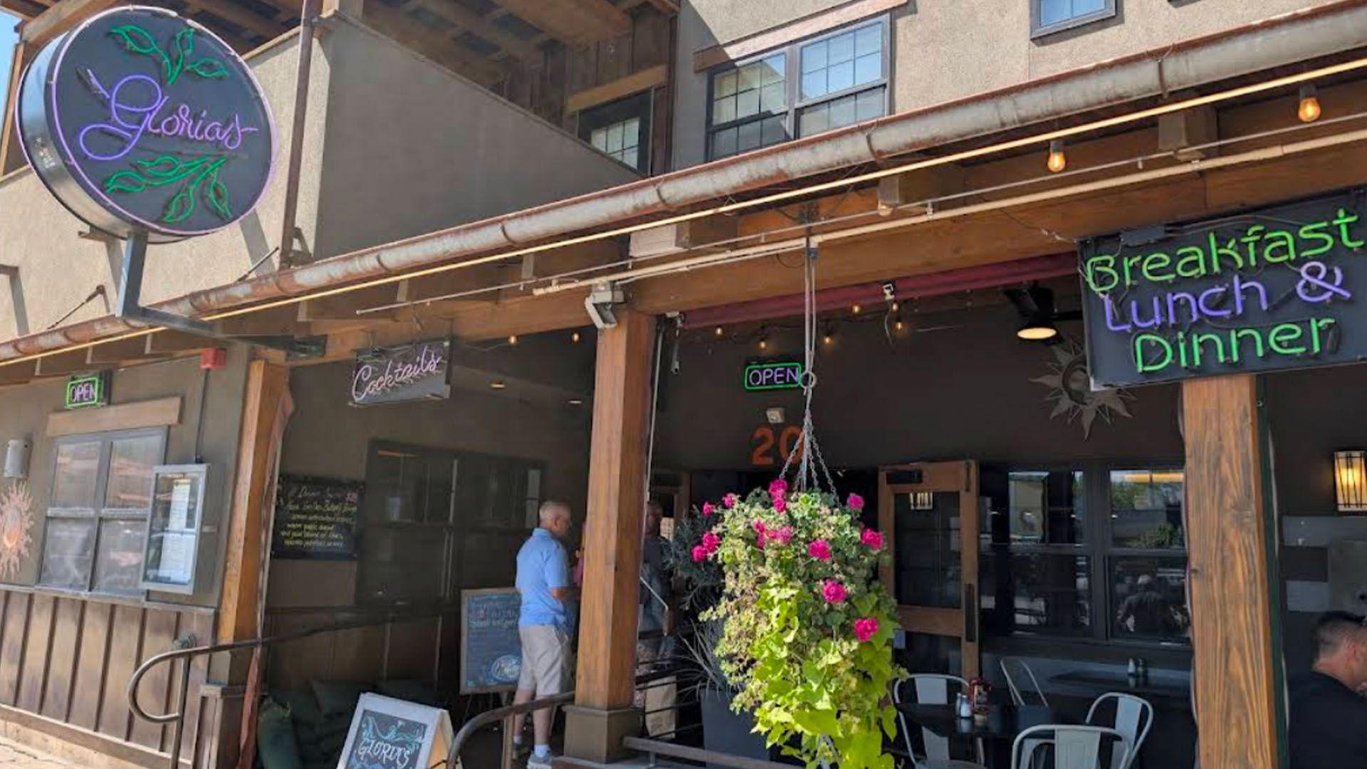 Exterior of Gloria's restaurant with a neon sign and flowers, offering breakfast, lunch, and dinner.